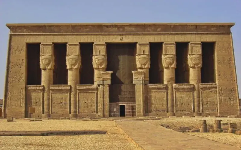 Approaching Dendera by Nile — the temple pylon visible as the lotus boat arrives by water